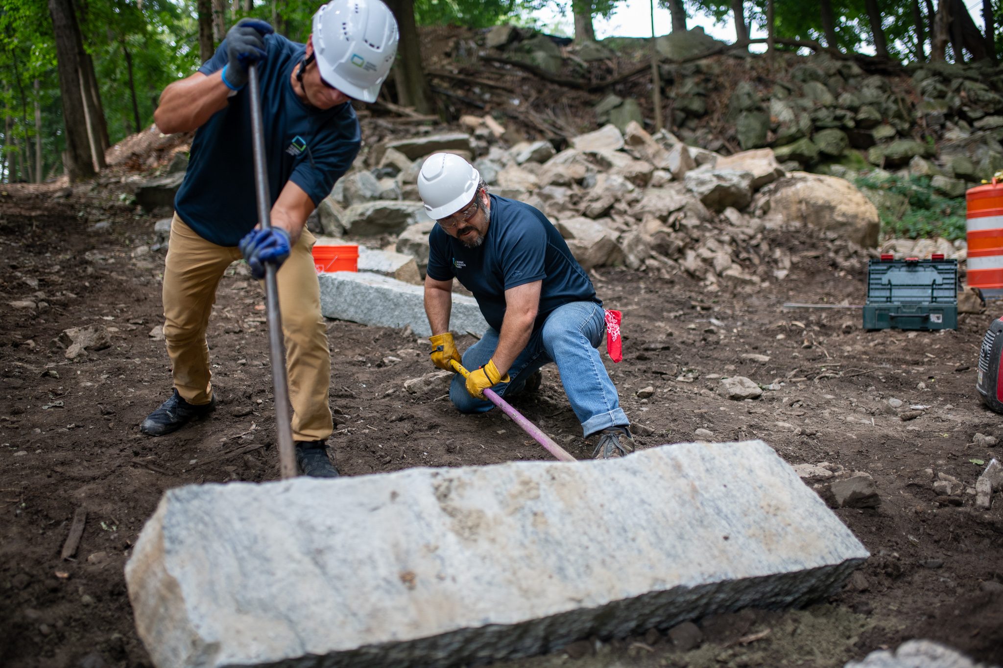 Two men bend over a long granite step, adjusting it by hand.