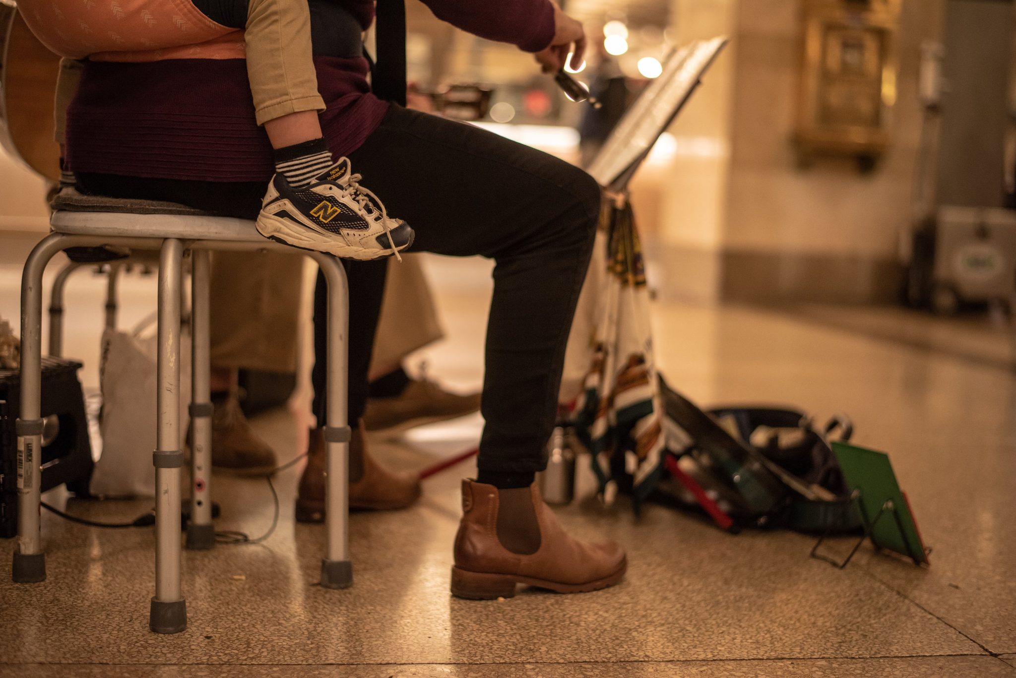 A small sneaker rests on Naomi's knee as she plays from her stool.