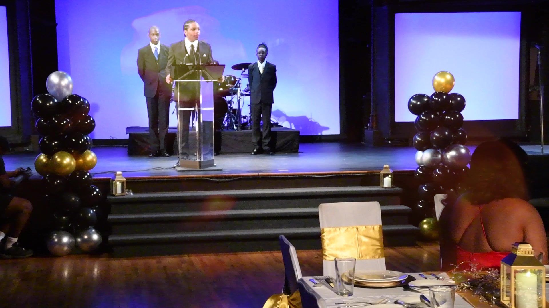 The stage between speeches, balloons in black and gold.