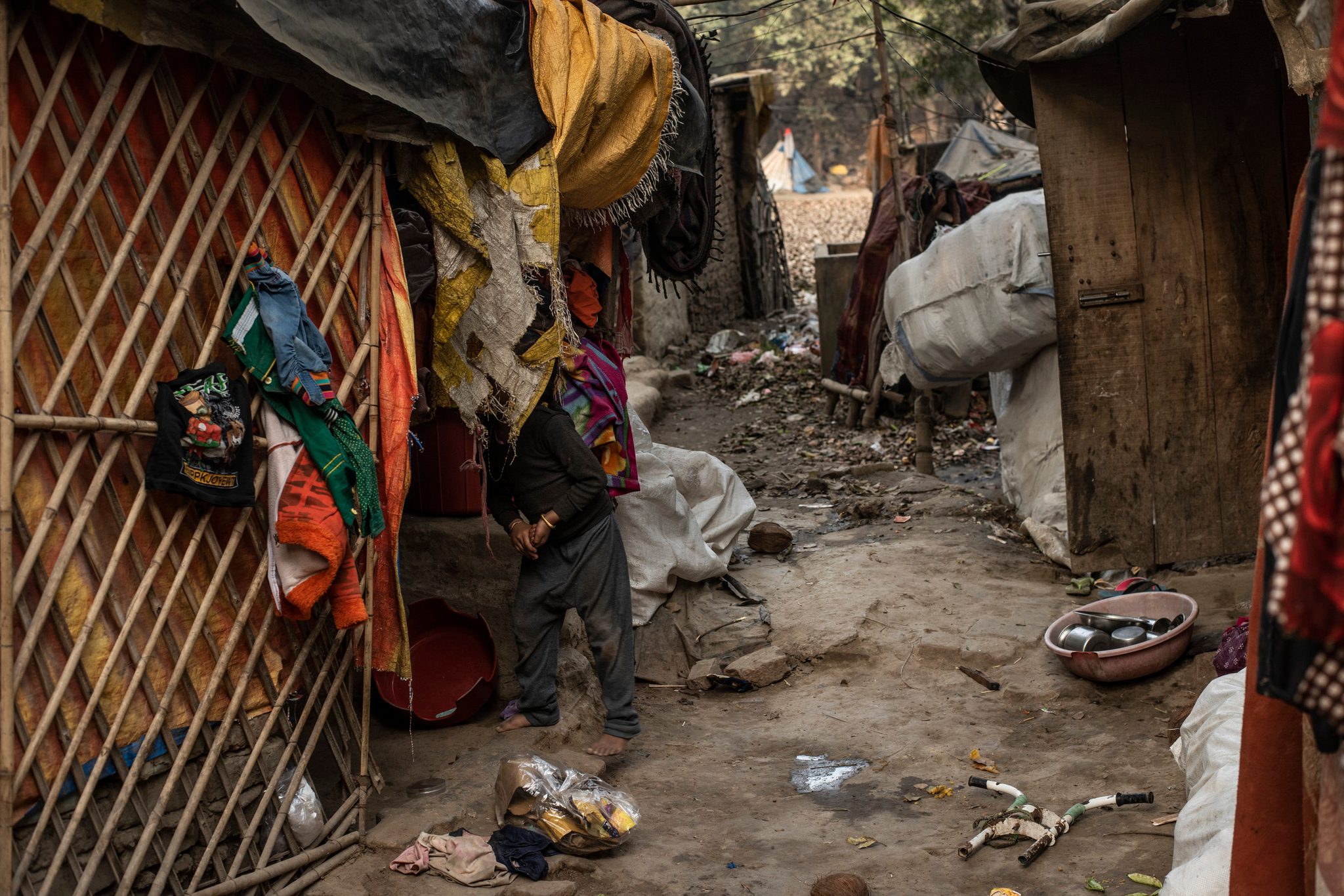 A child walks the narrow lane between makeshift shelters, laundry hung from every frame.