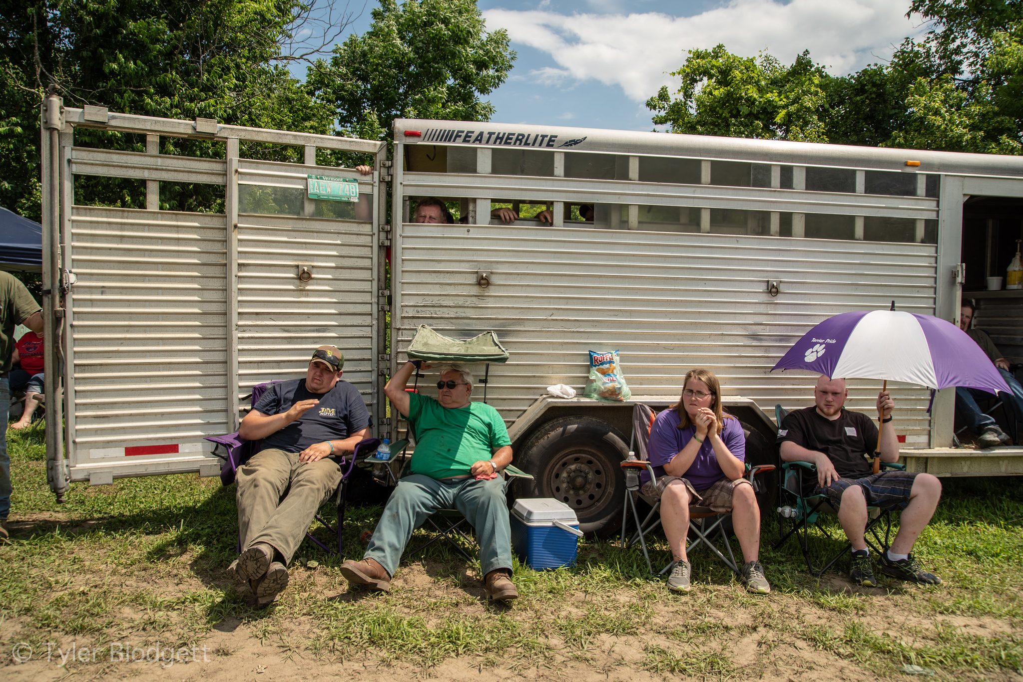 Spectators claim the only shade on the field, lined up against the horse trailer with a cooler at their feet.