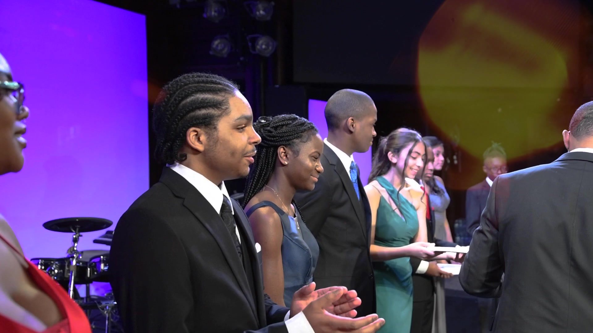 Graduates line up on stage in suits and gowns, certificates in hand.