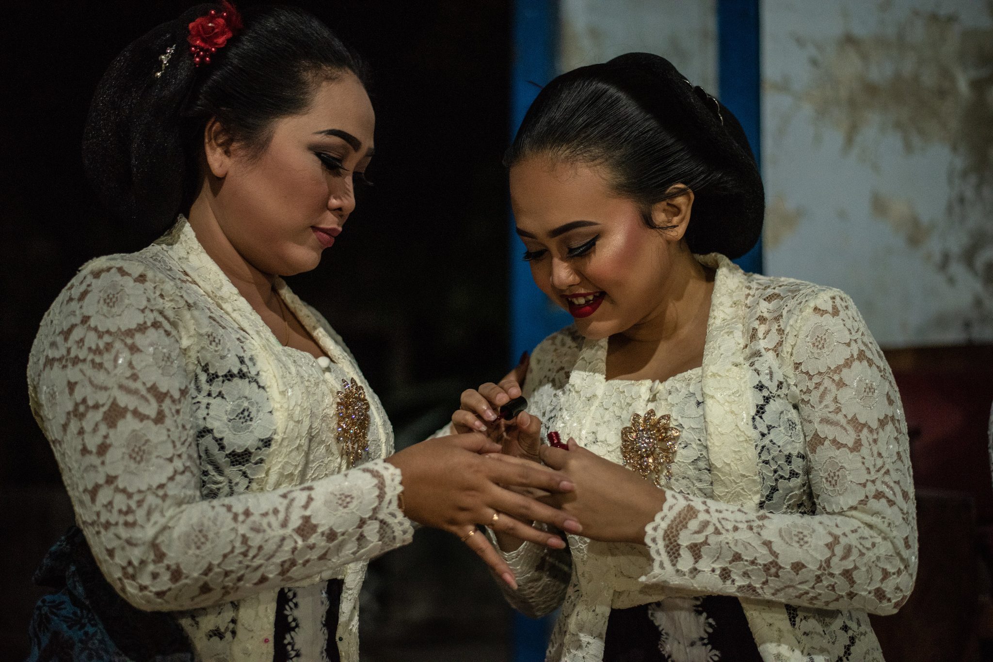 One singer paints the other's nails, both already dressed in lace for the show.