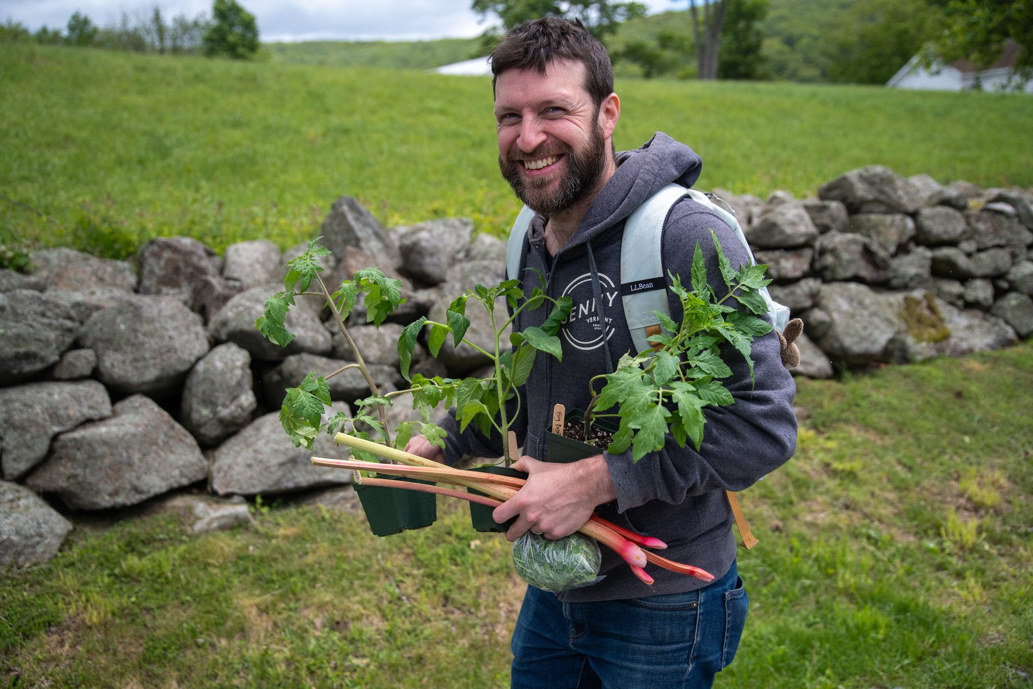 A man grins over an armful of plant starts and rhubarb.