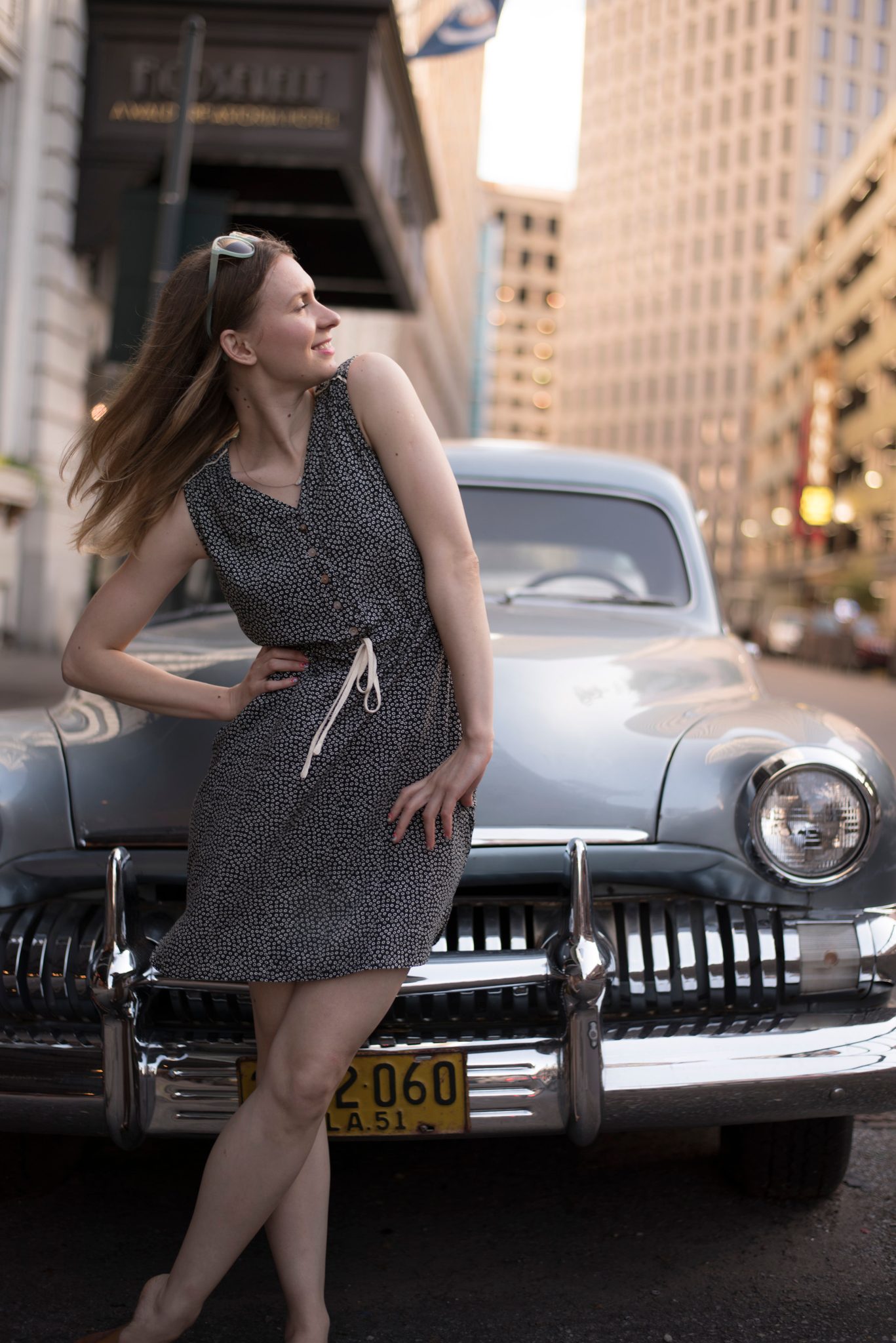 A soul stuck out of time leans against a vintage car. Face to the sky, she challenges the sun.
