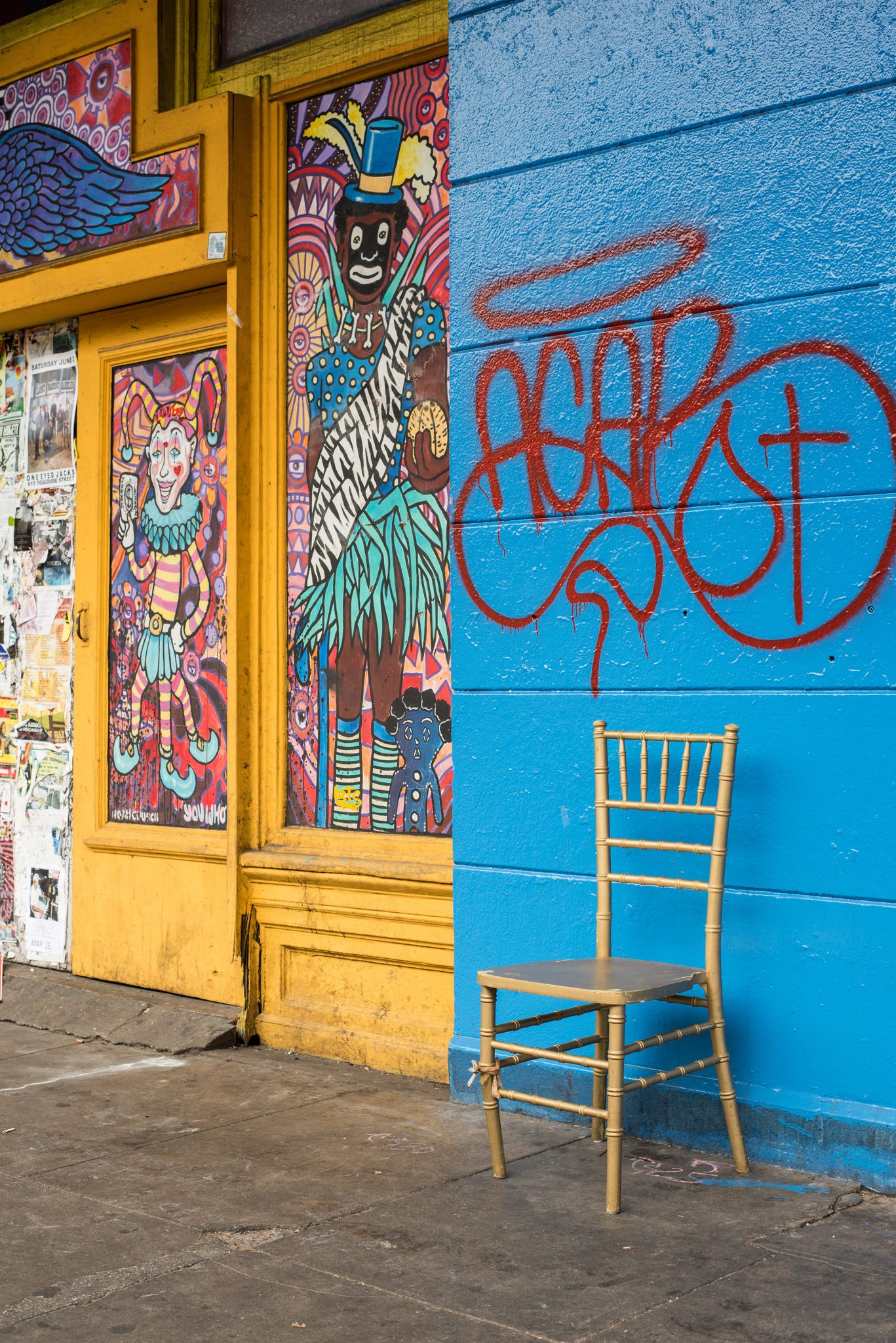 A gilded chair waits against a bright blue wall beside a painted door, a throne for whoever claims it.
