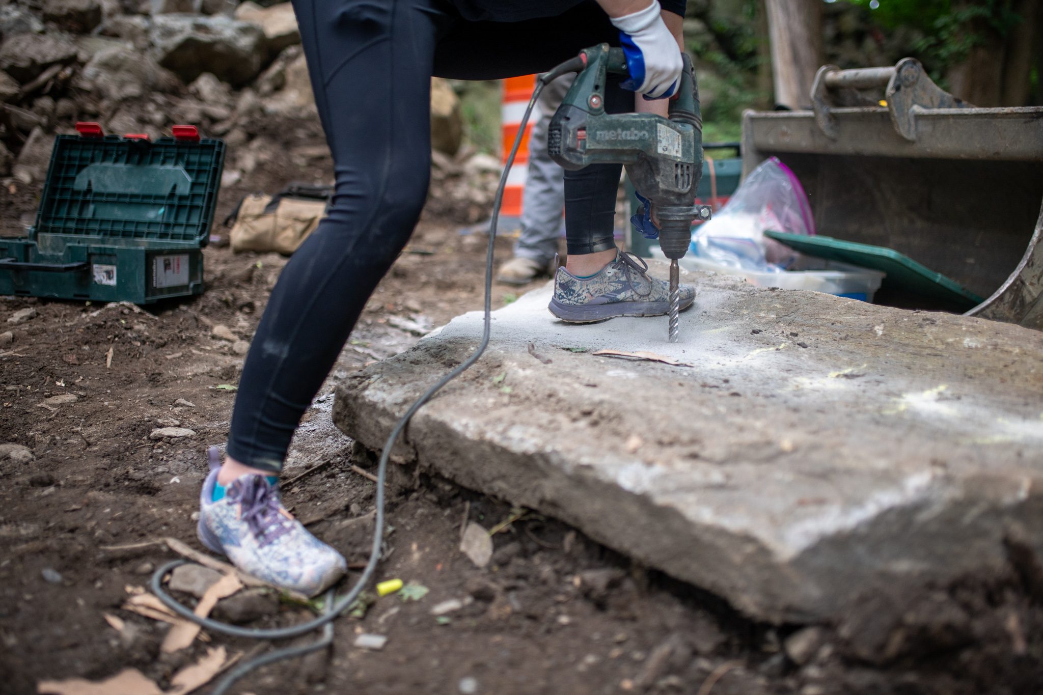 A drill stands upright in a slab as she leans into it.