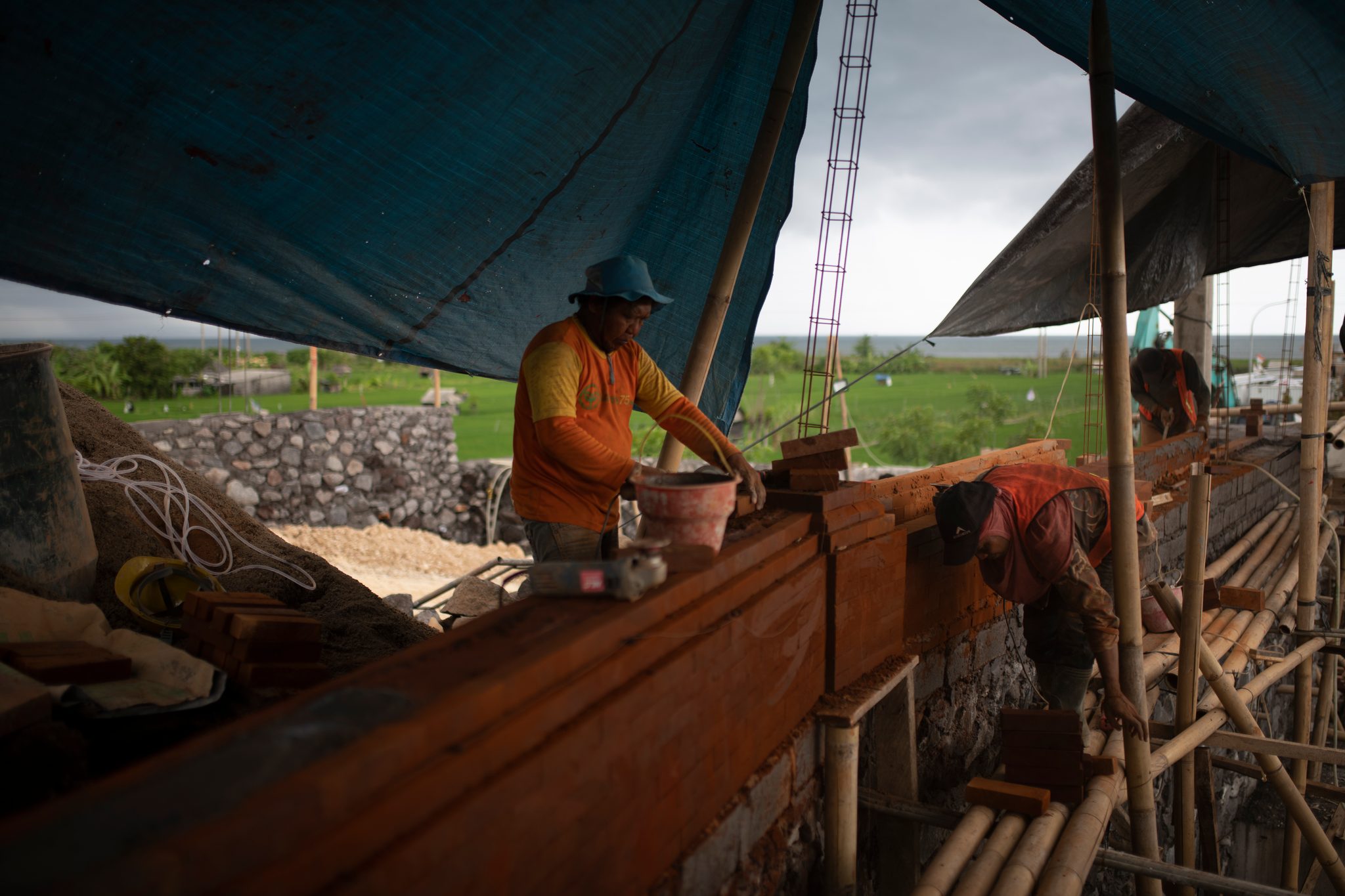 Two workers shape material along the trough as the storm clouds build.