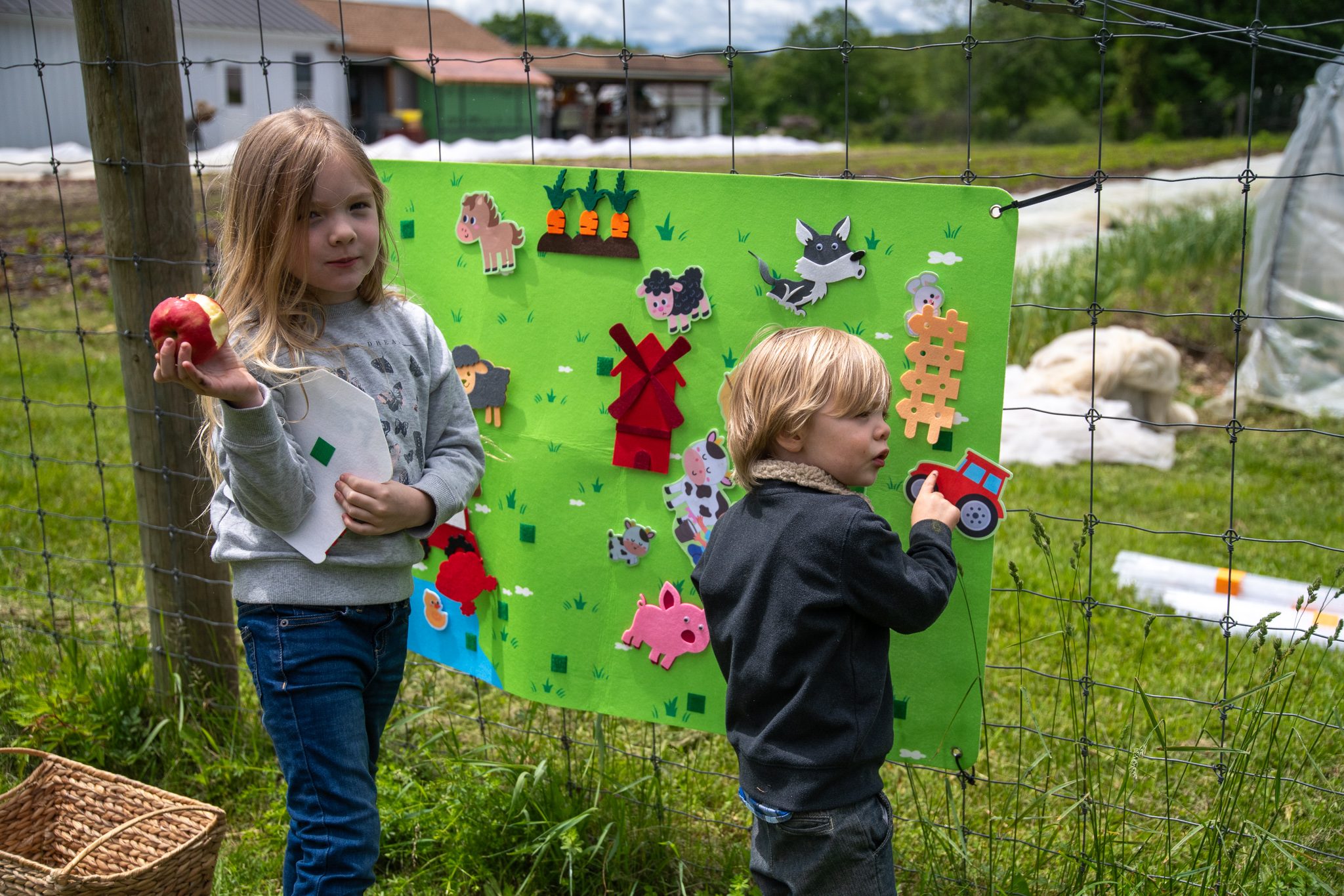 Apple in hand, a girl looks up while her little brother finds a place for his felt tractor.