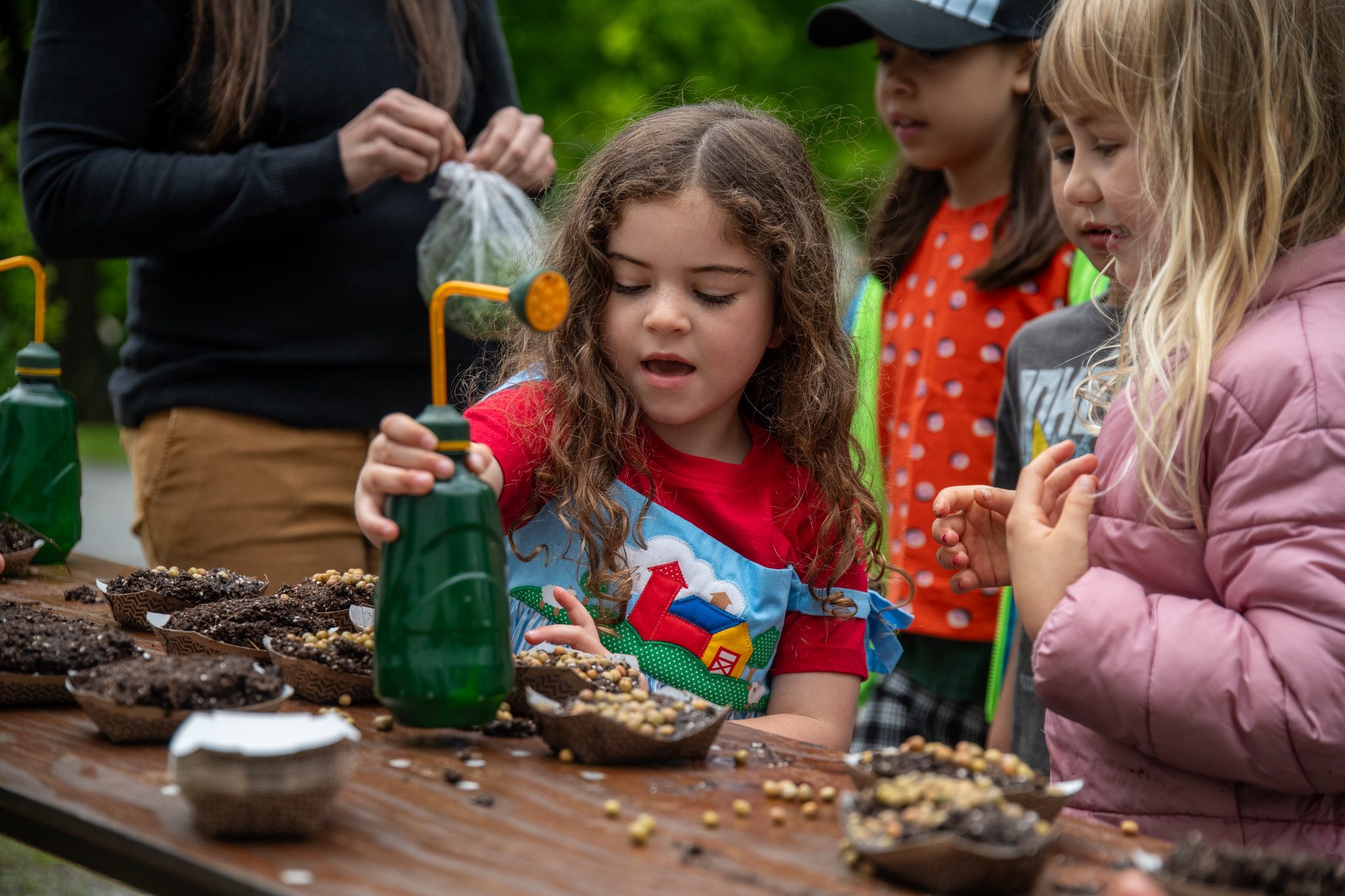 A girl waters the seeds she just pressed into the soil.