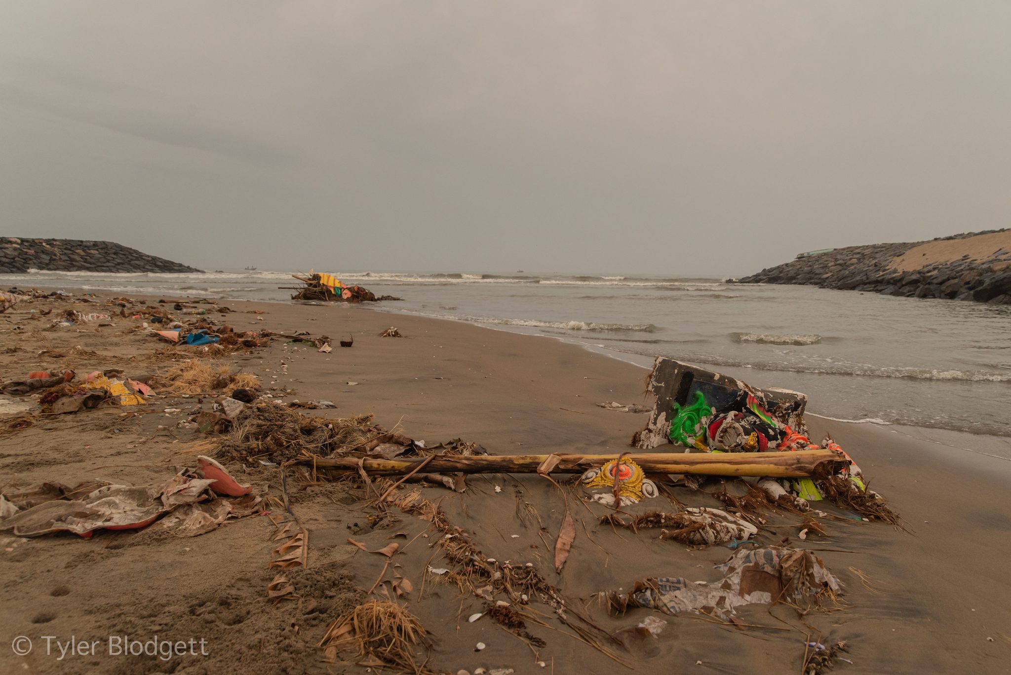 Bamboo, marigolds and bright scraps lie washed up on the sand.