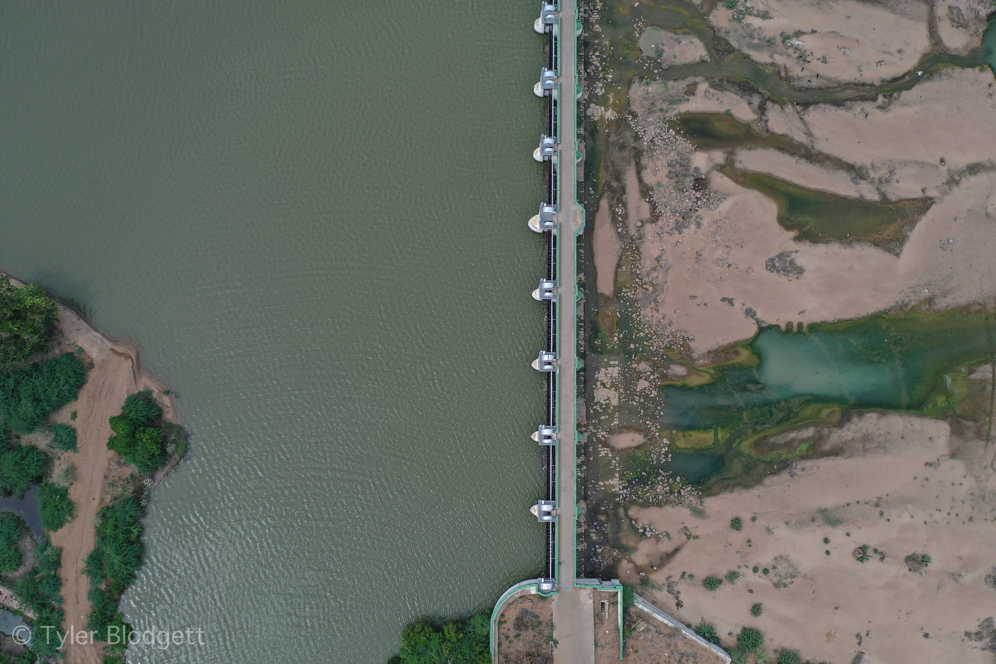 A barrage cuts across the frame, deep water on one side and sand on the other.