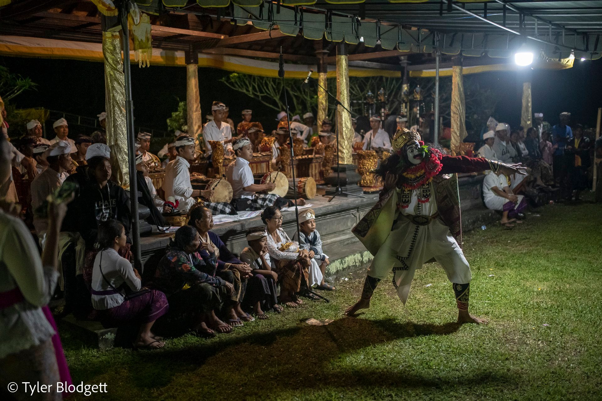 After dark, a masked dancer lunges across the grass while the gamelan plays under the lights.