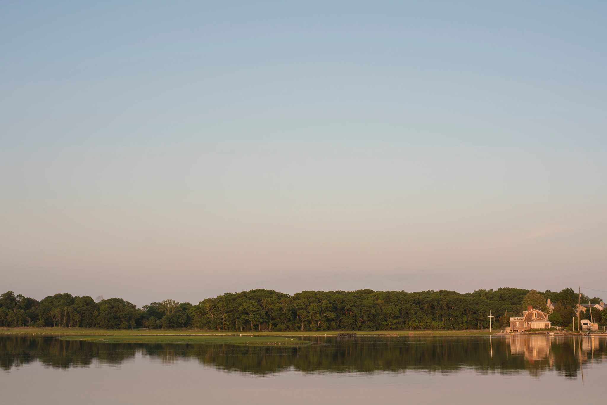 The shore goes still at dusk, trees and sky mirrored in the flat water.