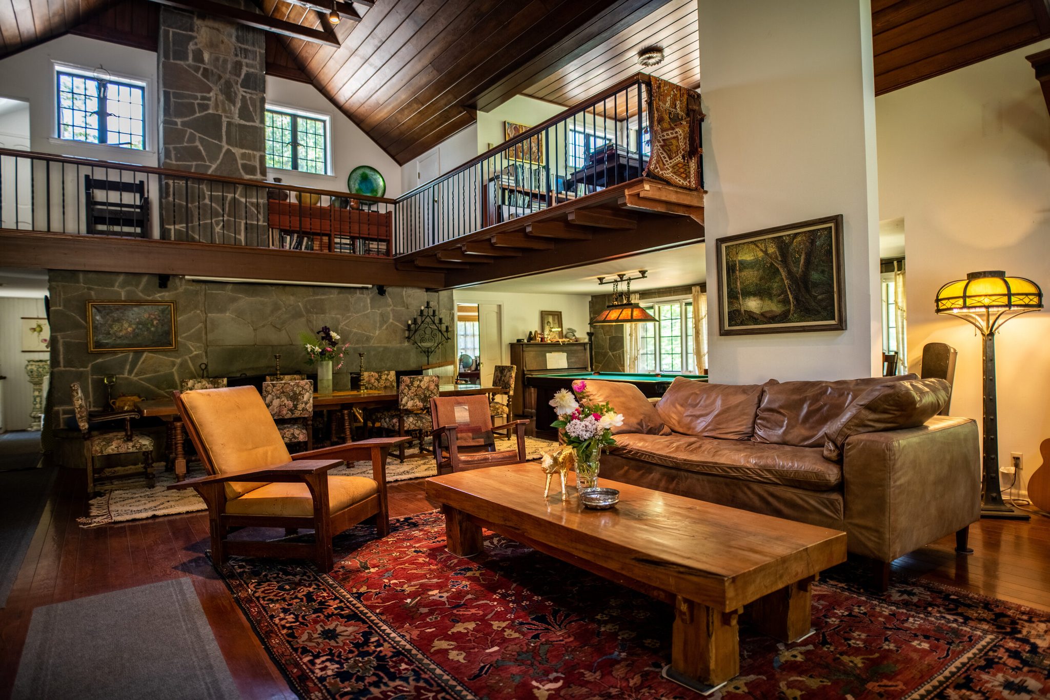 A stone chimney rises two stories past the balcony, the lamps lit in the great room below.