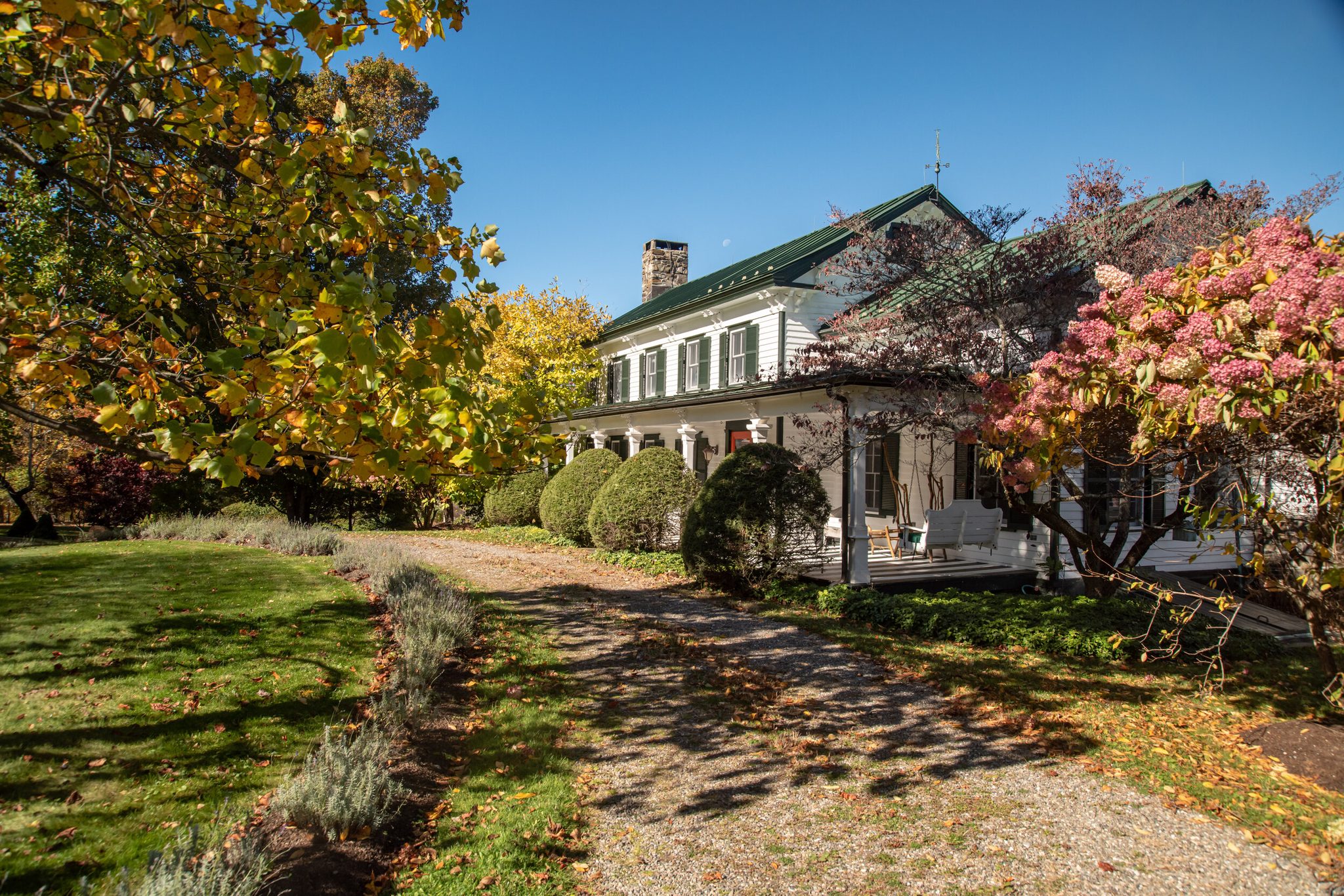 A gravel drive curves toward the farmhouse through a yard full of fall color.