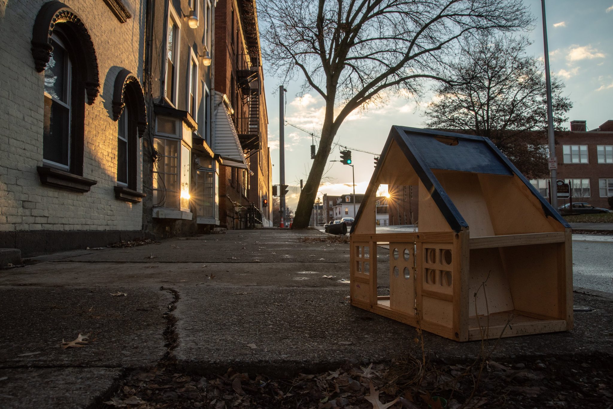 A wooden dollhouse sits on the sidewalk, catching the last of the sun.