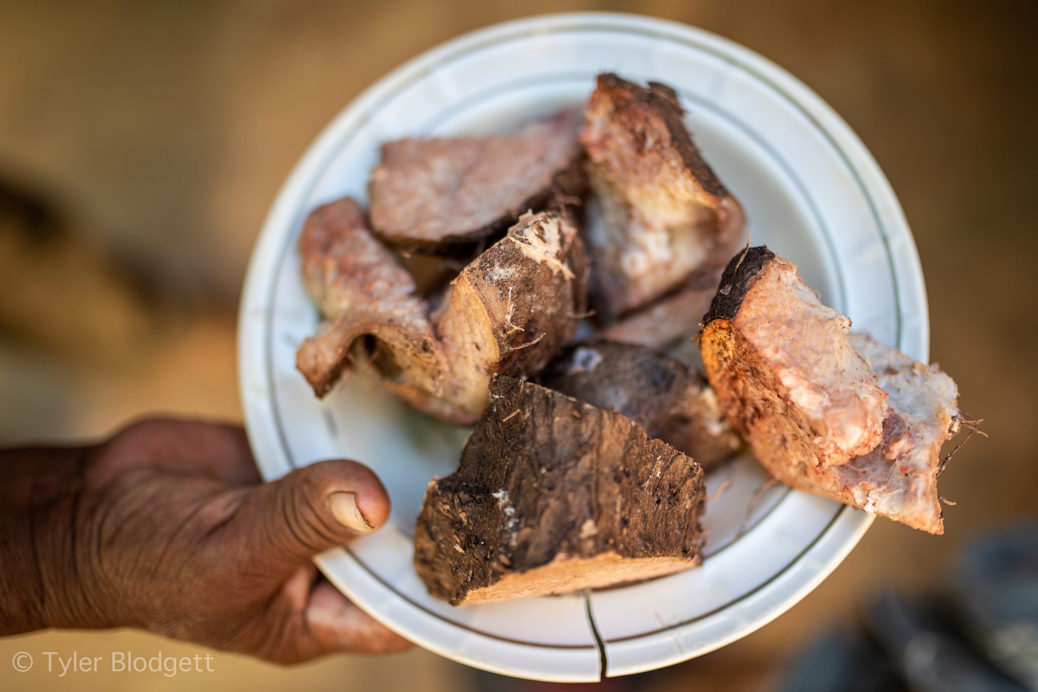 A weathered hand holds out a plate of meat fresh from the fire.