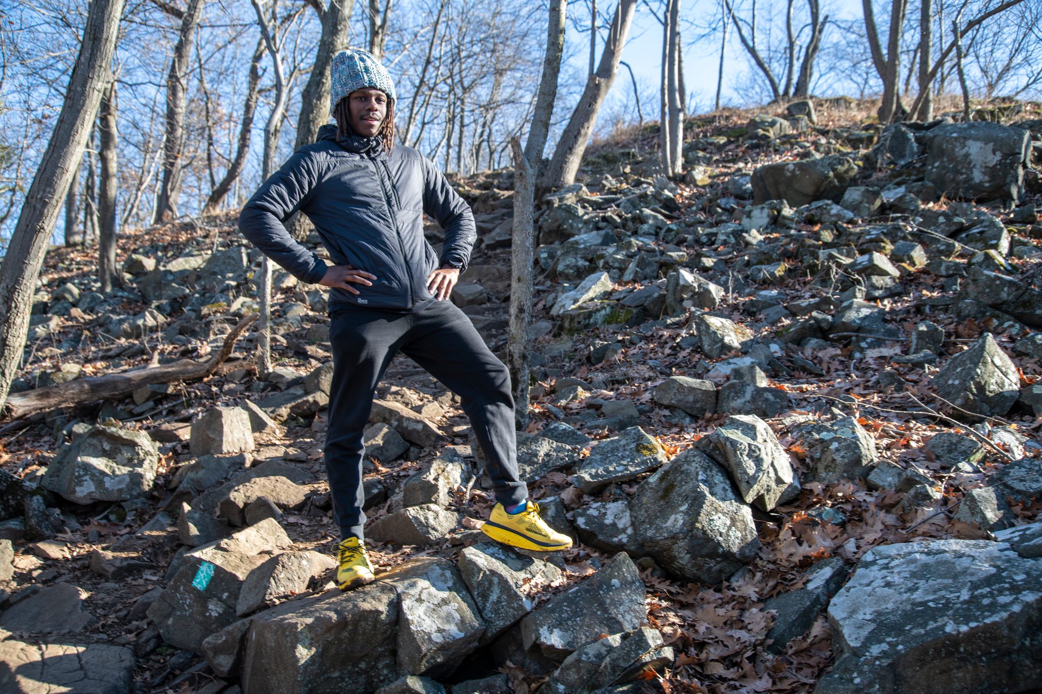 Hands on hips halfway up a boulder slope, Chev takes a breath among the bare trees.