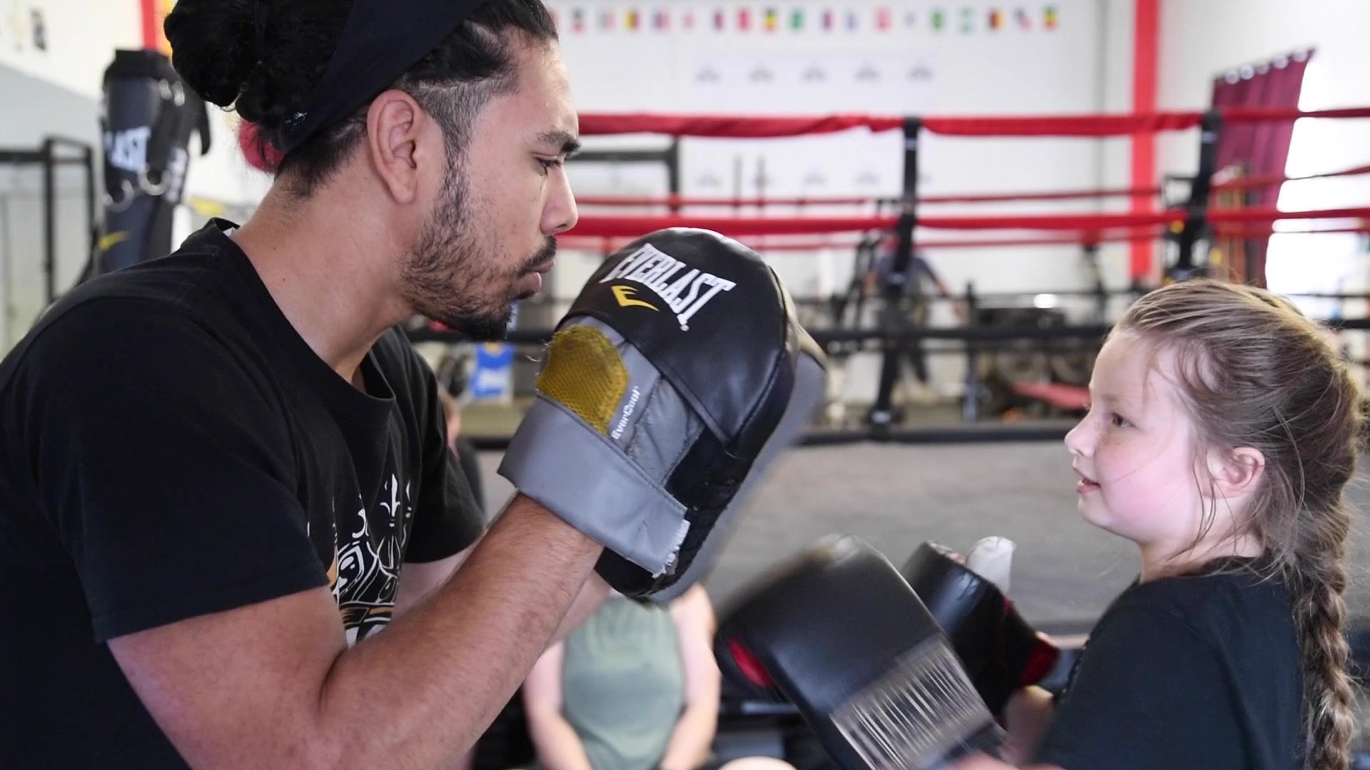 A small boxer in braids squares up to the mitts, gloves nearly as big as her head.