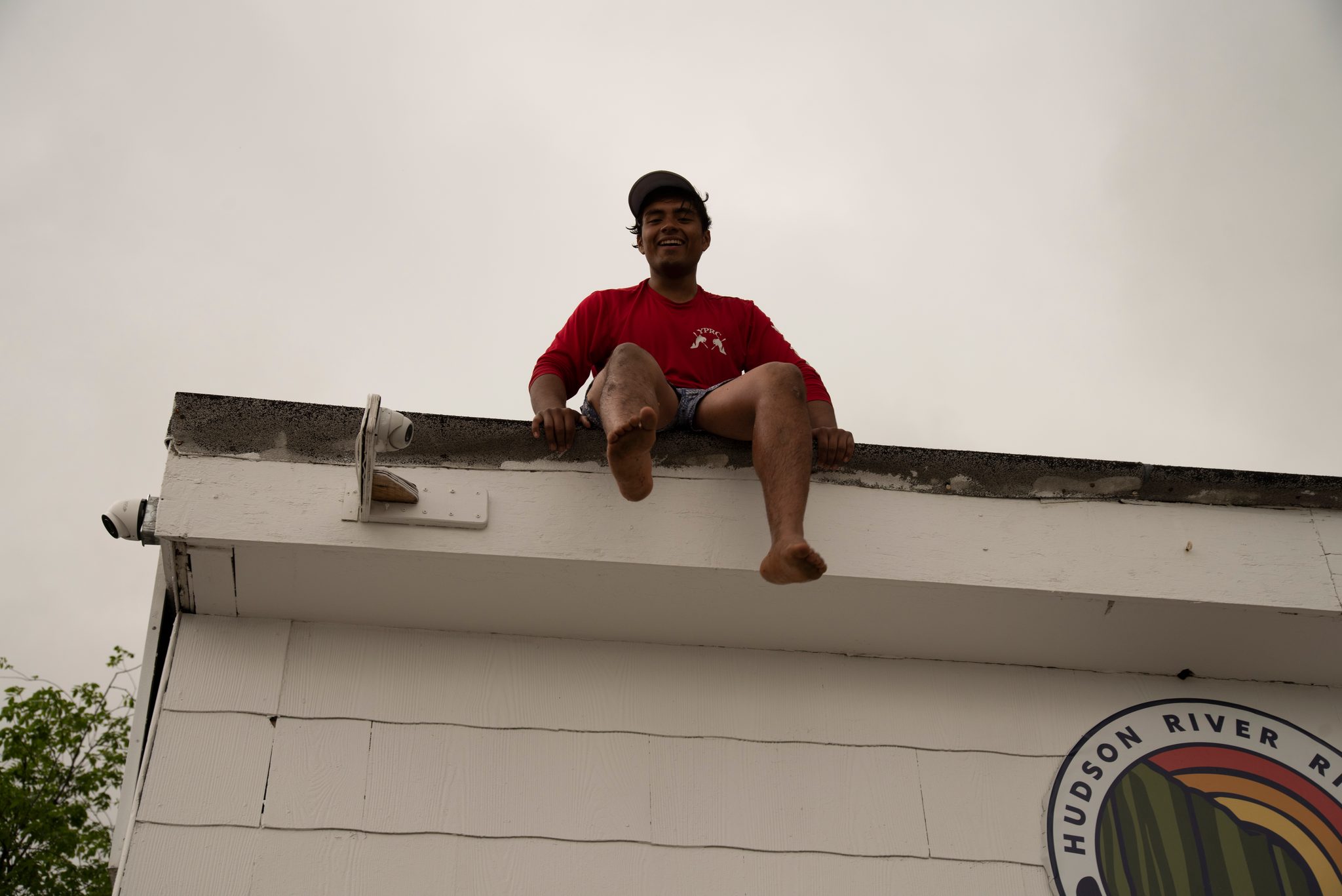 Someone has climbed onto the boathouse roof for a better view, legs dangling over the edge.