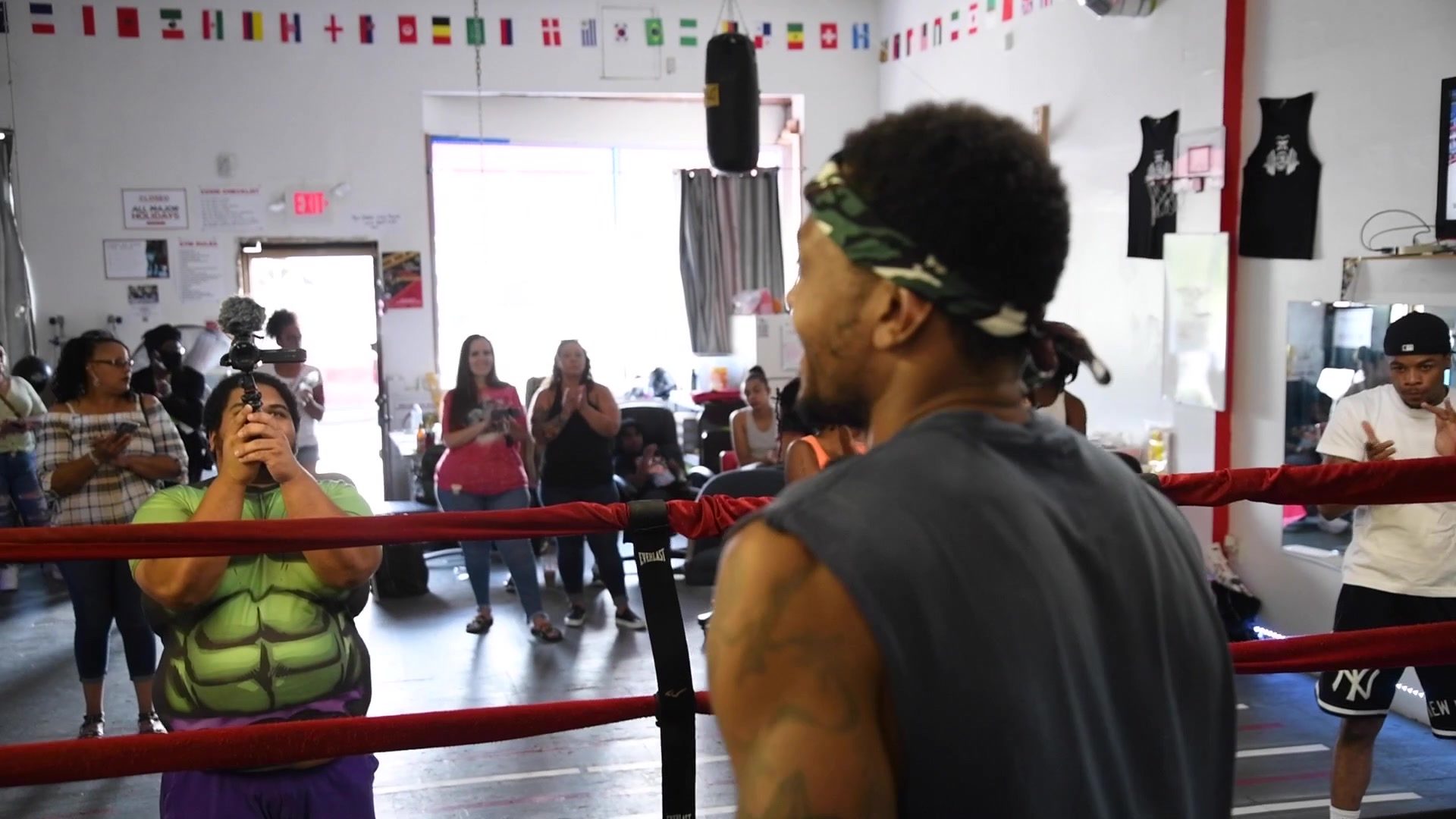 Phones up around the ring as a boxer in a headband squares off, a spectator in a green superhero shirt among them.