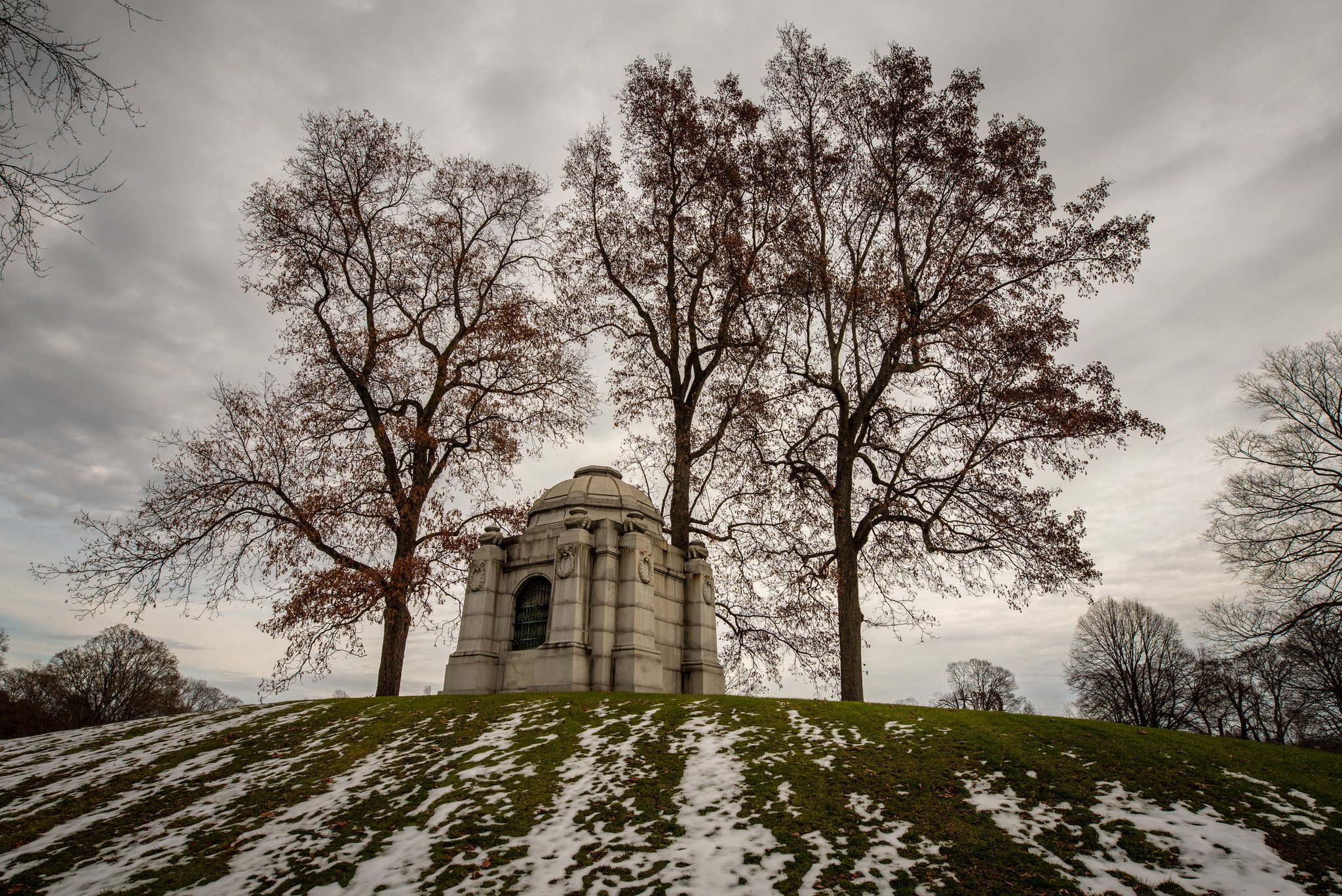 A stone mausoleum crowns the hill beneath bare trees, the snow melting back into the grass. May my life mean more than words on a headstone.