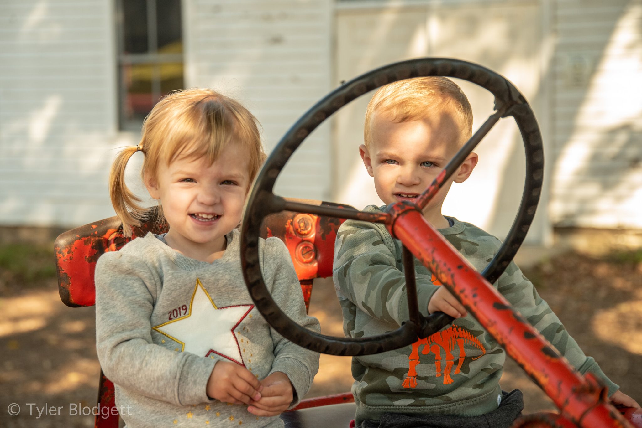 Two toddlers take the wheel of an old red tractor, neither one ready to give it up.