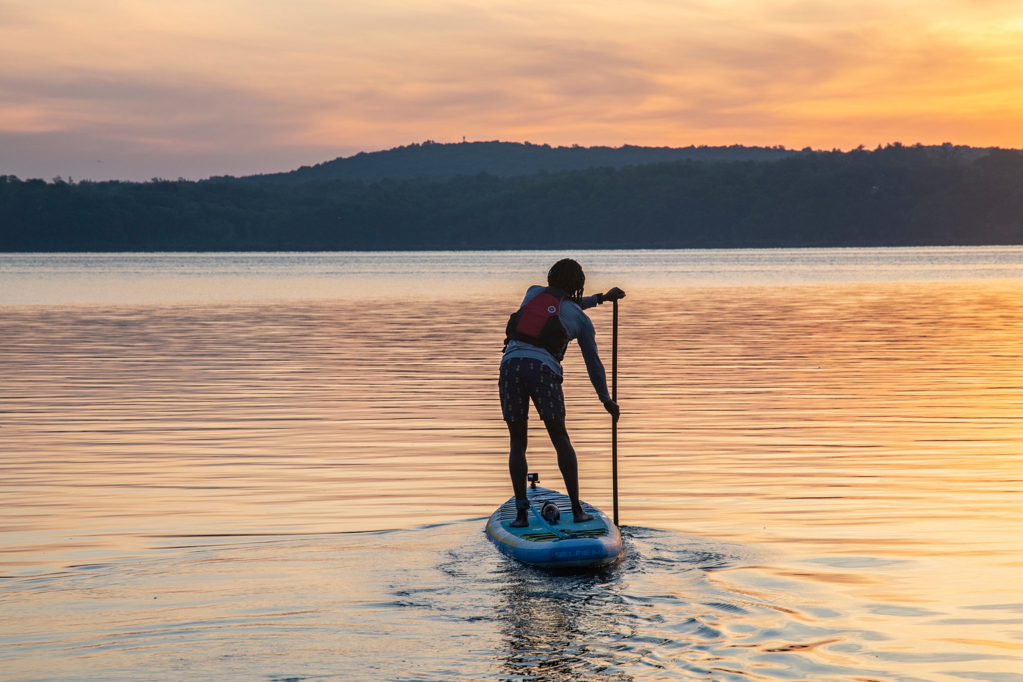 Seen from behind, Chev paddles into water gone orange and lavender at dawn.