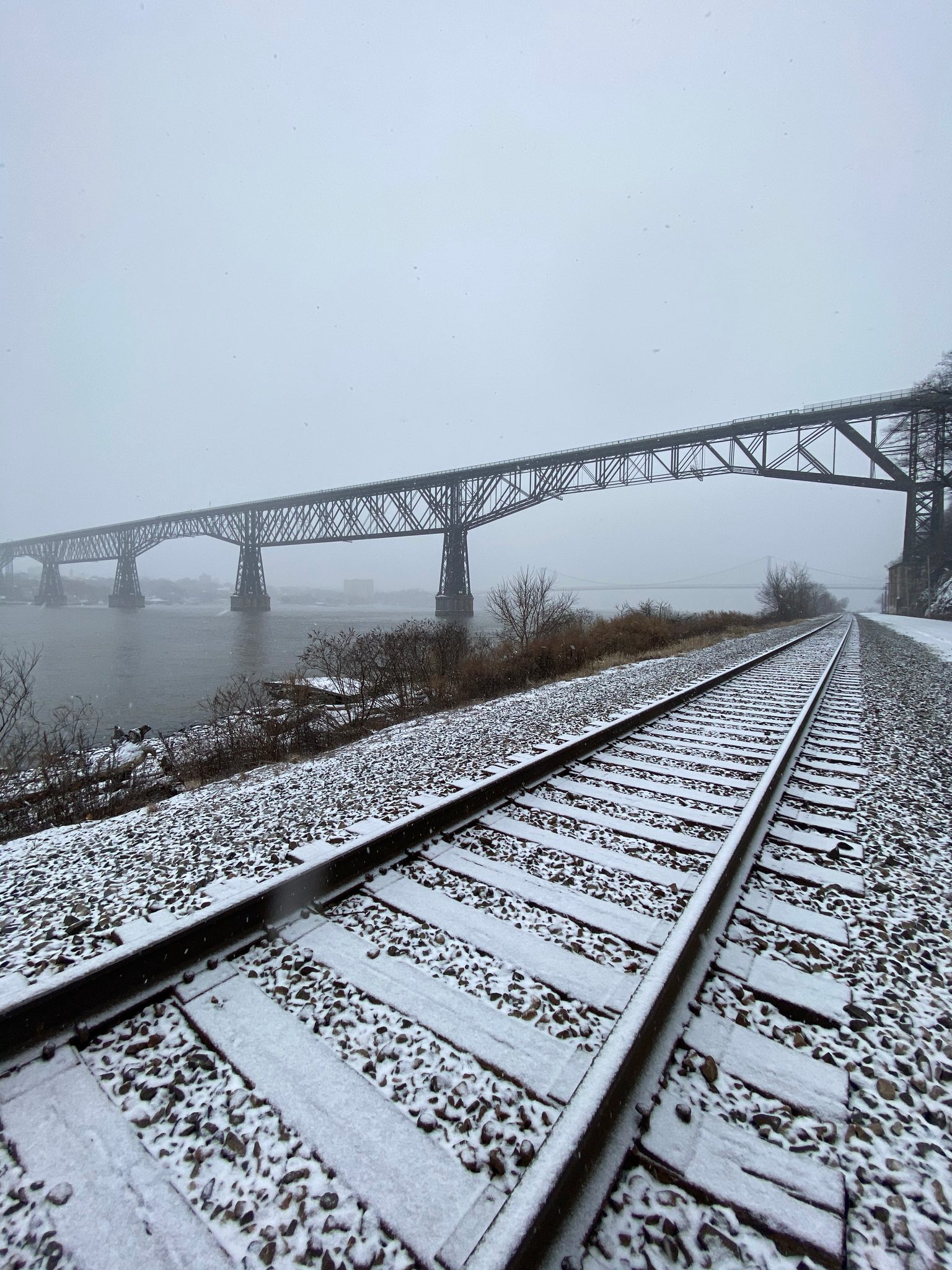 Snow on the rail line along the river, the Walkway lost in fog beyond.