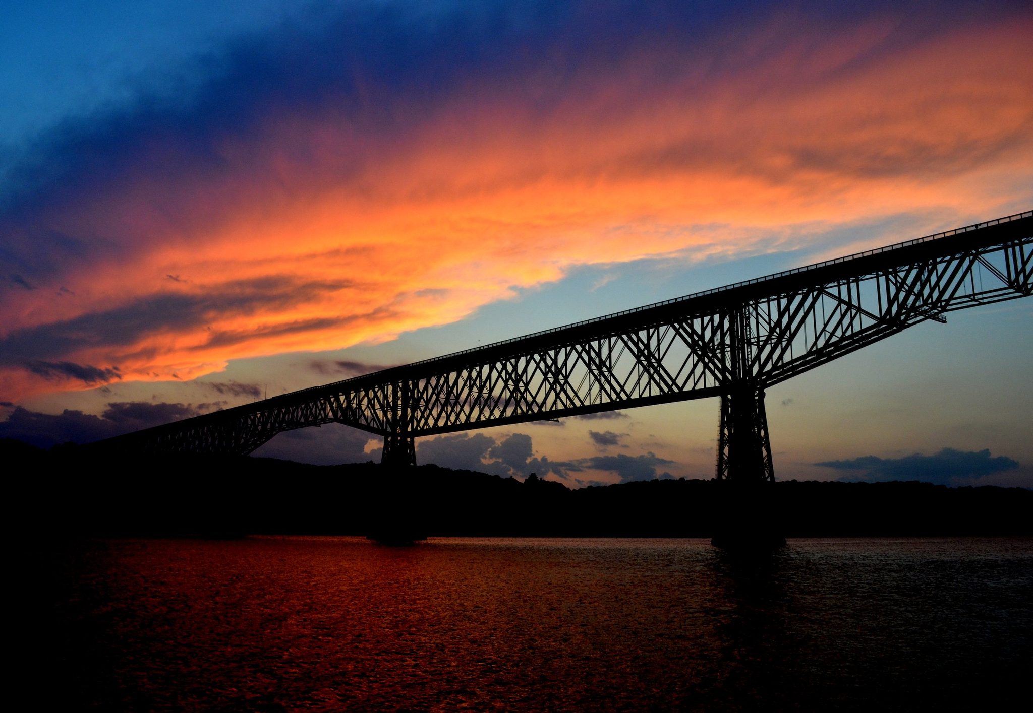 The railroad bridge cuts a black silhouette across a burning sky.