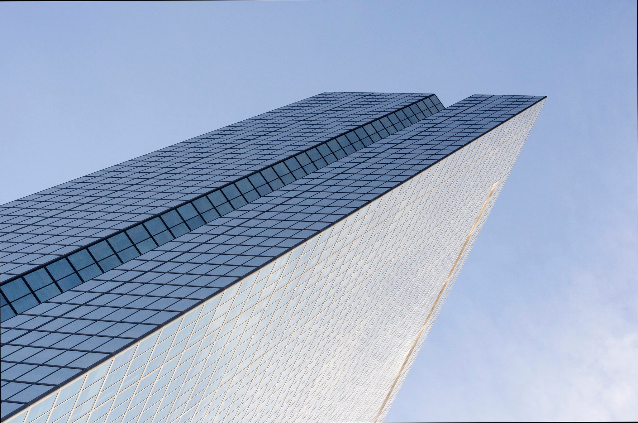 A glass tower rises straight into the blue.