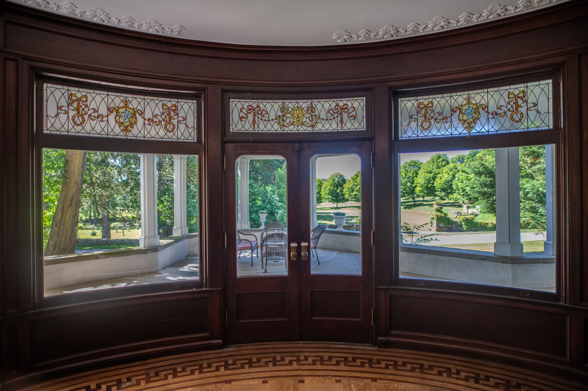 The curved bay seen straight on, ribbon-and-garland glass above the windows and French doors out to the porch.