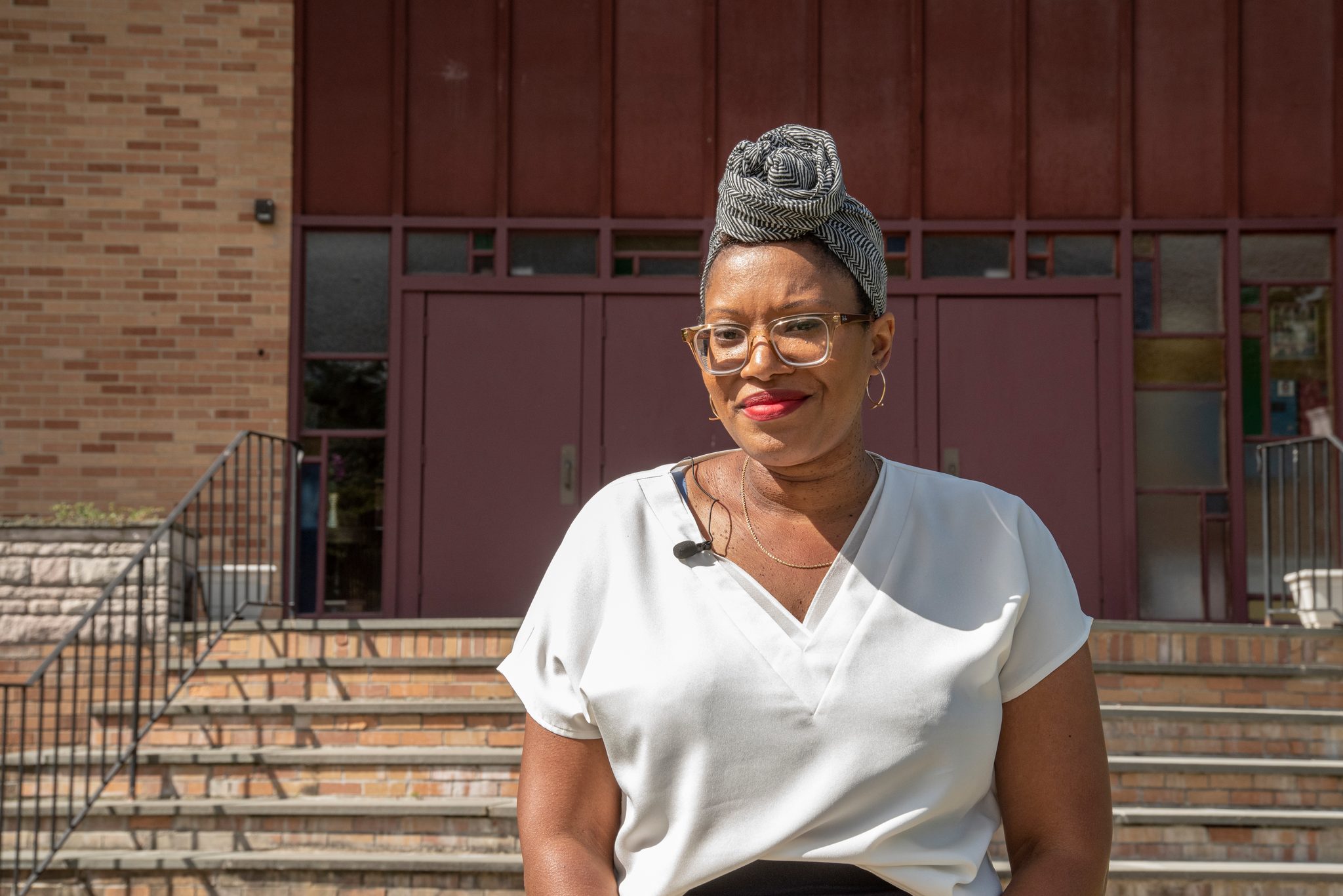 A woman smiles on the church steps, head wrapped in silver.