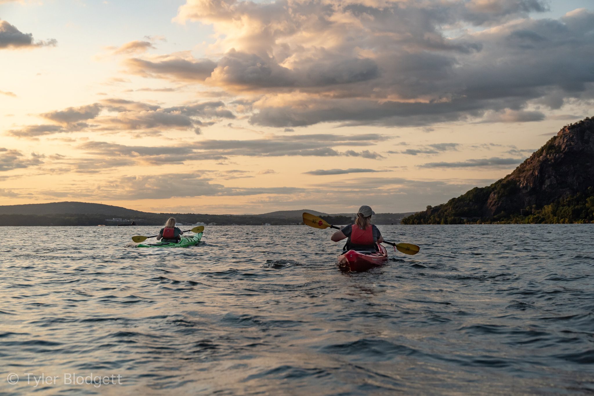 Two kayakers paddle out into the evening glow, the mountain shouldering up on the right.