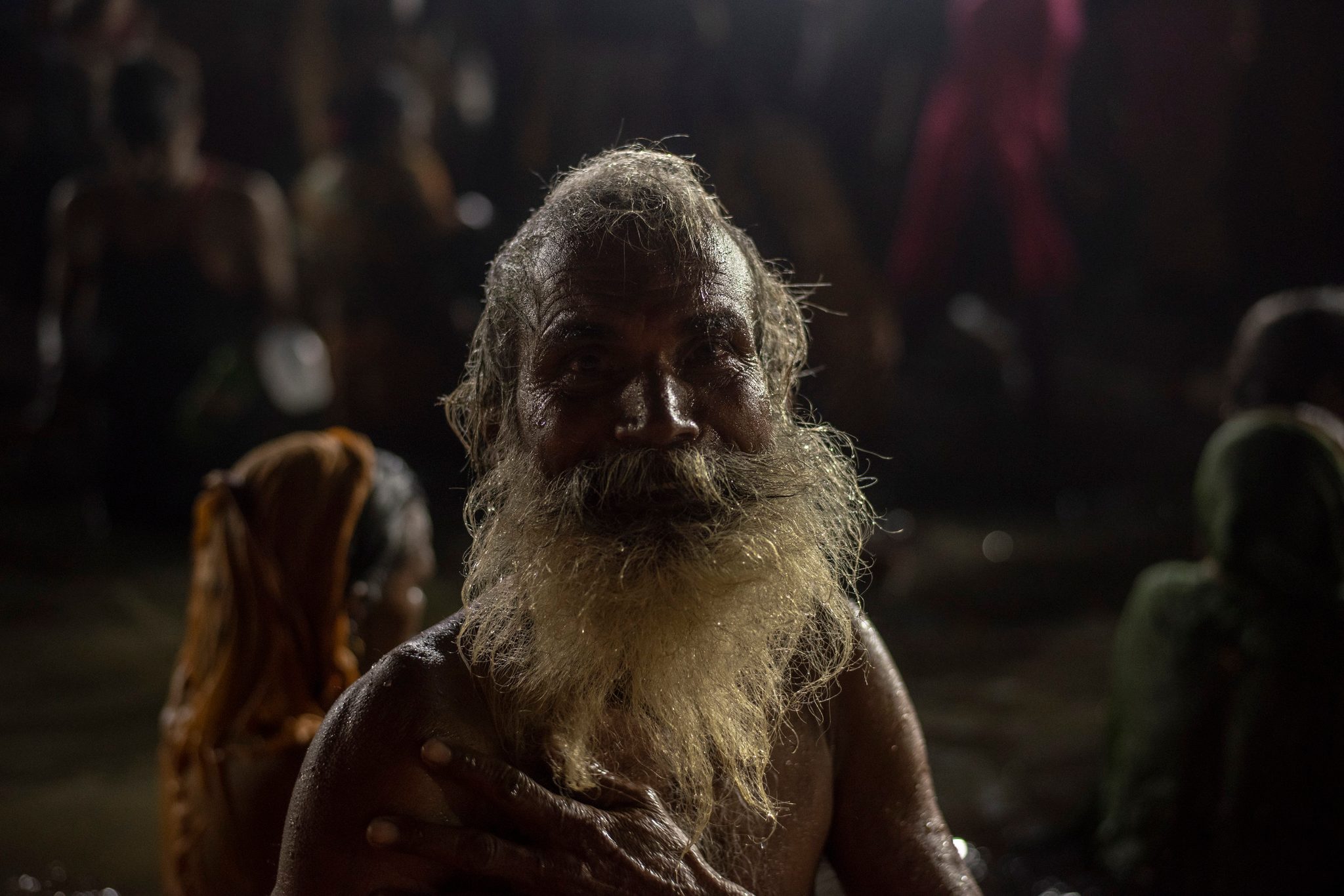 An elder with a white beard rises from the water, one hand pressed to his chest.
