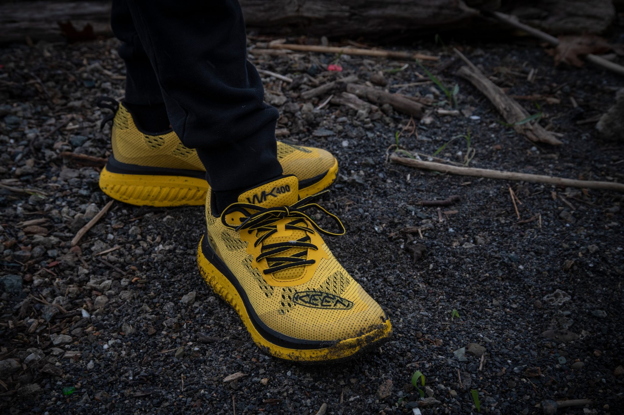Yellow shoes on black gravel and wet twigs, laces pulled tight for a cold December walk.