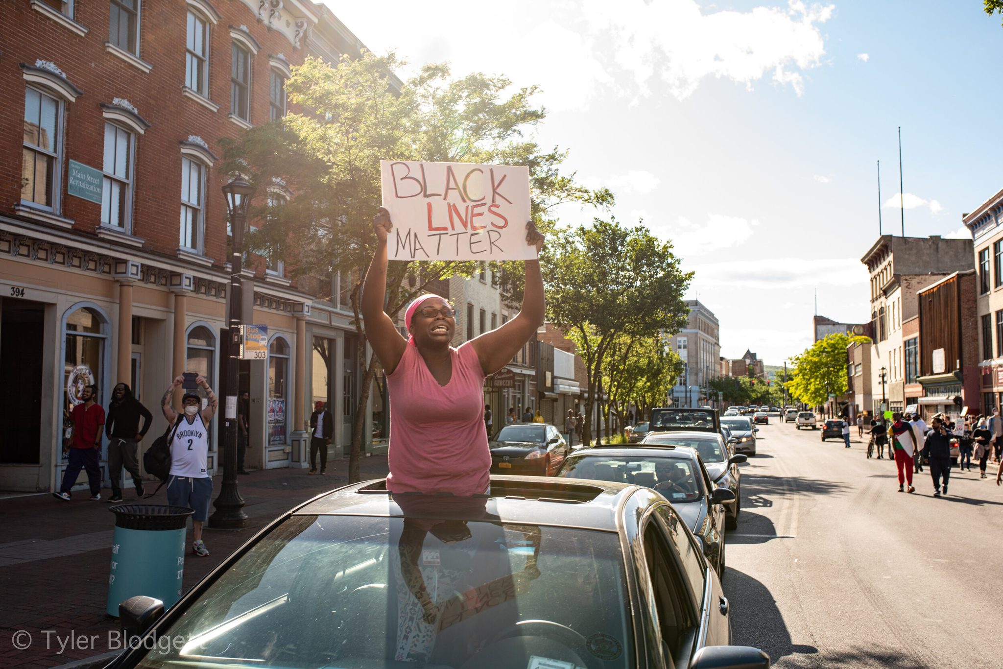 A woman rises through a sunroof with a Black Lives Matter sign as the march fills the downtown street.